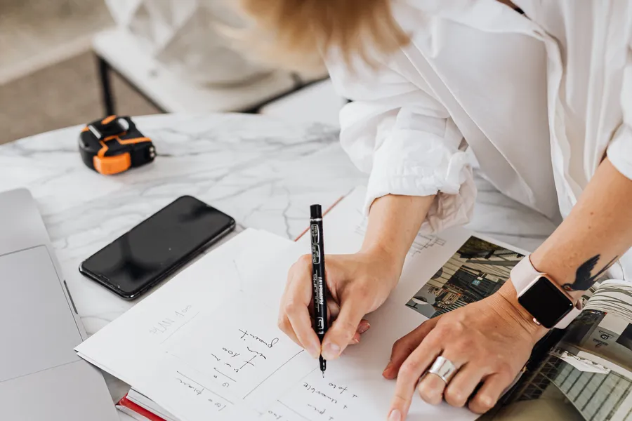 Notebook, house plans, keys, and coffee on a well-lit worktable