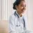 Black&nbsp;female&nbsp;doctor&nbsp;smiling&nbsp;at&nbsp;desk&nbsp;with&nbsp;stethoscope,&nbsp;in&nbsp;a&nbsp;bright&nbsp;medical&nbsp;office.