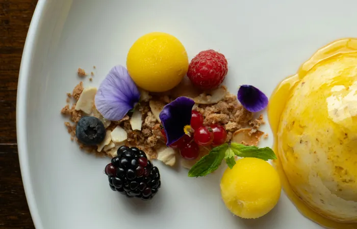 A&nbsp;beautifully&nbsp;plated&nbsp;dessert&nbsp;with&nbsp;mango&nbsp;sorbet,&nbsp;fresh&nbsp;berries,&nbsp;and&nbsp;edible&nbsp;flowers.