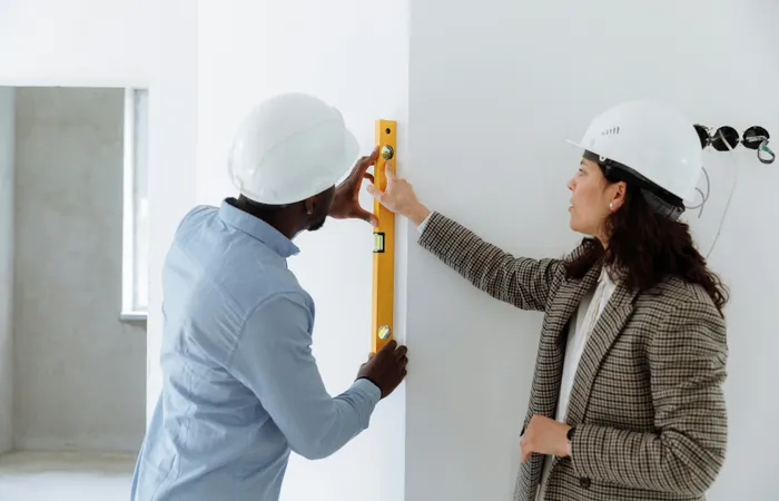 Two&nbsp;contractors&nbsp;using&nbsp;a&nbsp;level&nbsp;bar&nbsp;to&nbsp;check&nbsp;wall&nbsp;alignment&nbsp;inside&nbsp;a&nbsp;building.