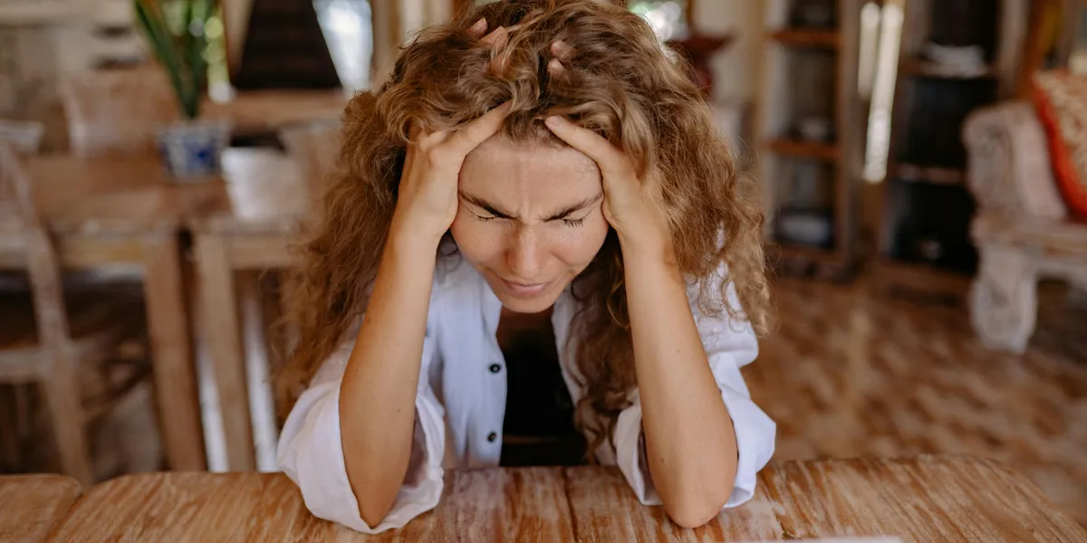 A&nbsp;stressed&nbsp;woman&nbsp;sits&nbsp;at&nbsp;a&nbsp;wooden&nbsp;table,&nbsp;frustrated&nbsp;with&nbsp;her&nbsp;laptop&nbsp;work.