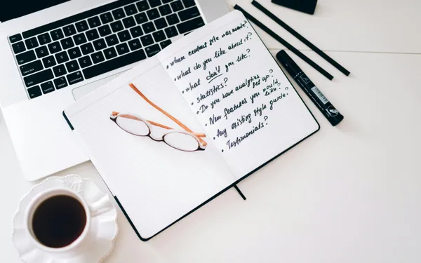 A&nbsp;stylish&nbsp;workspace&nbsp;featuring&nbsp;a&nbsp;laptop,&nbsp;notebook&nbsp;with&nbsp;notes,&nbsp;glasses,&nbsp;and&nbsp;a&nbsp;coffee&nbsp;cup.
