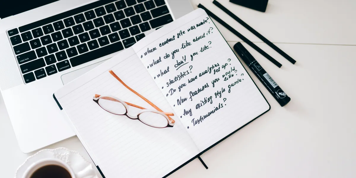 A&nbsp;stylish&nbsp;workspace&nbsp;featuring&nbsp;a&nbsp;laptop,&nbsp;notebook&nbsp;with&nbsp;notes,&nbsp;glasses,&nbsp;and&nbsp;a&nbsp;coffee&nbsp;cup.