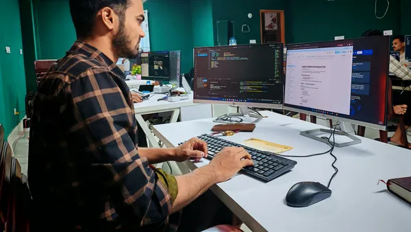 A&nbsp;software&nbsp;developer&nbsp;working&nbsp;on&nbsp;code&nbsp;at&nbsp;a&nbsp;dual&nbsp;monitor&nbsp;setup&nbsp;in&nbsp;a&nbsp;modern&nbsp;office.