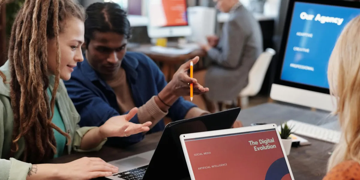 Diverse&nbsp;team&nbsp;collaborating&nbsp;with&nbsp;laptops&nbsp;in&nbsp;a&nbsp;modern&nbsp;office&nbsp;setting,&nbsp;discussing&nbsp;digital&nbsp;evolution.