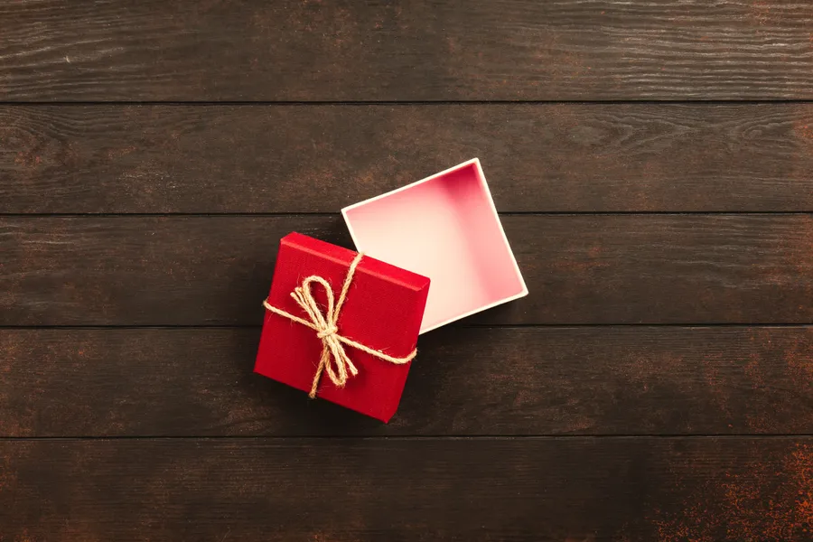 Top&nbsp;view&nbsp;of&nbsp;an&nbsp;open&nbsp;red&nbsp;gift&nbsp;box&nbsp;tied&nbsp;with&nbsp;twine&nbsp;on&nbsp;a&nbsp;wooden&nbsp;surface.