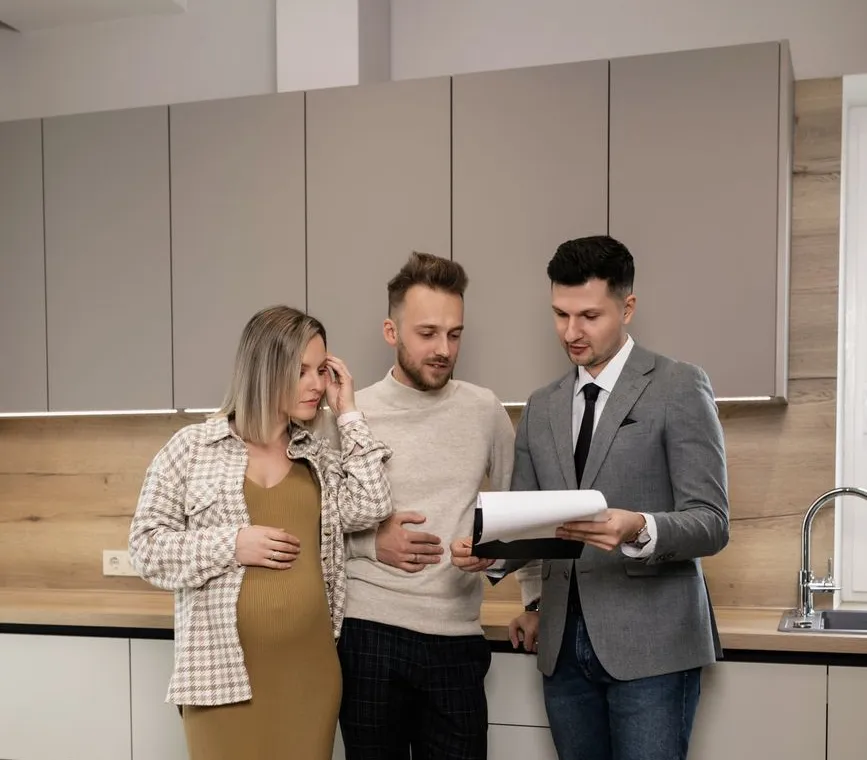 A&nbsp;real&nbsp;estate&nbsp;professional&nbsp;talks&nbsp;through&nbsp;house&nbsp;plans&nbsp;with&nbsp;clients&nbsp;at&nbsp;a&nbsp;kitchen&nbsp;table.