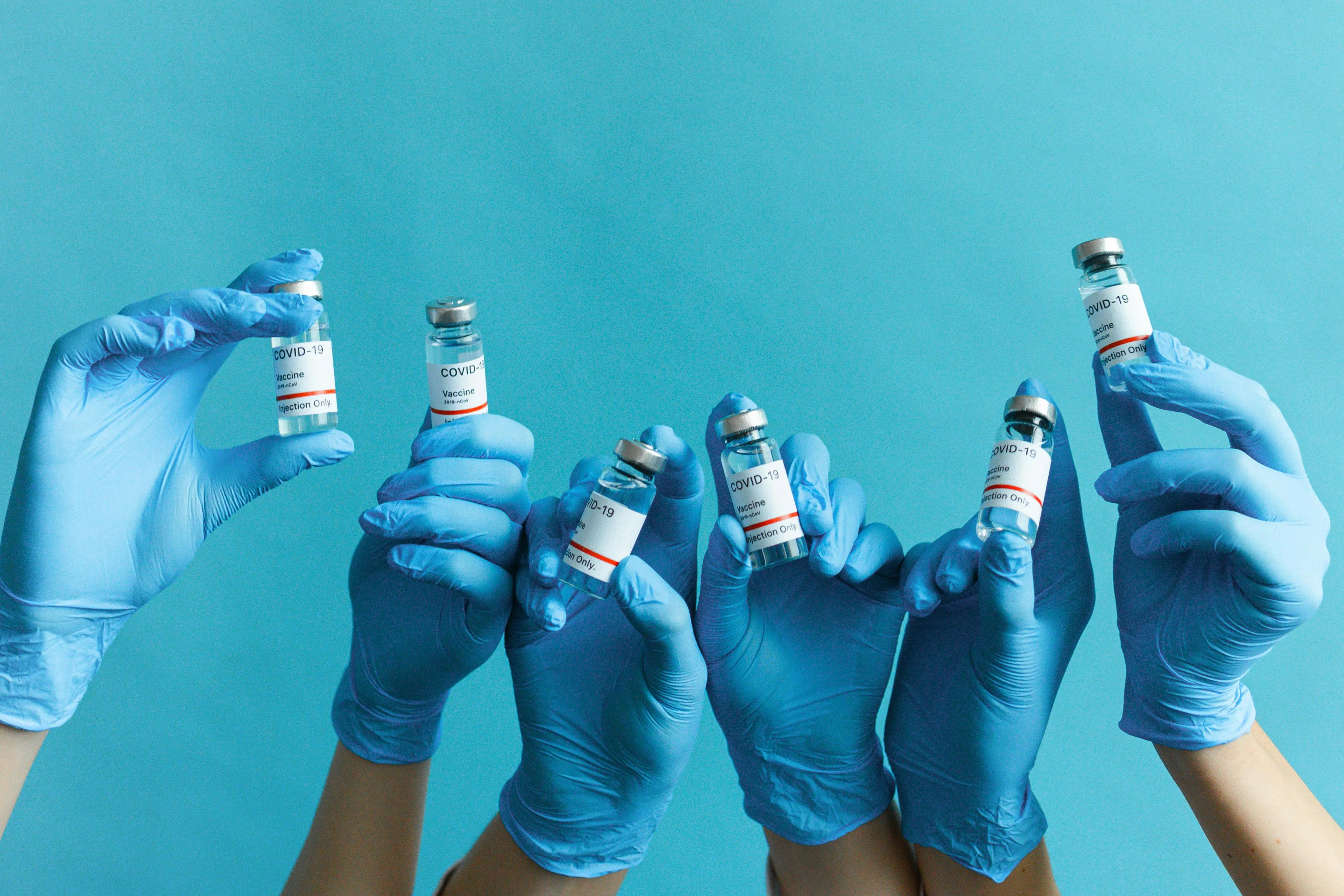 Hands&nbsp;in&nbsp;blue&nbsp;gloves&nbsp;holding&nbsp;COVID-19&nbsp;vaccine&nbsp;vials&nbsp;on&nbsp;a&nbsp;blue&nbsp;background,&nbsp;signifying&nbsp;immunization&nbsp;and&nbsp;healthcare.