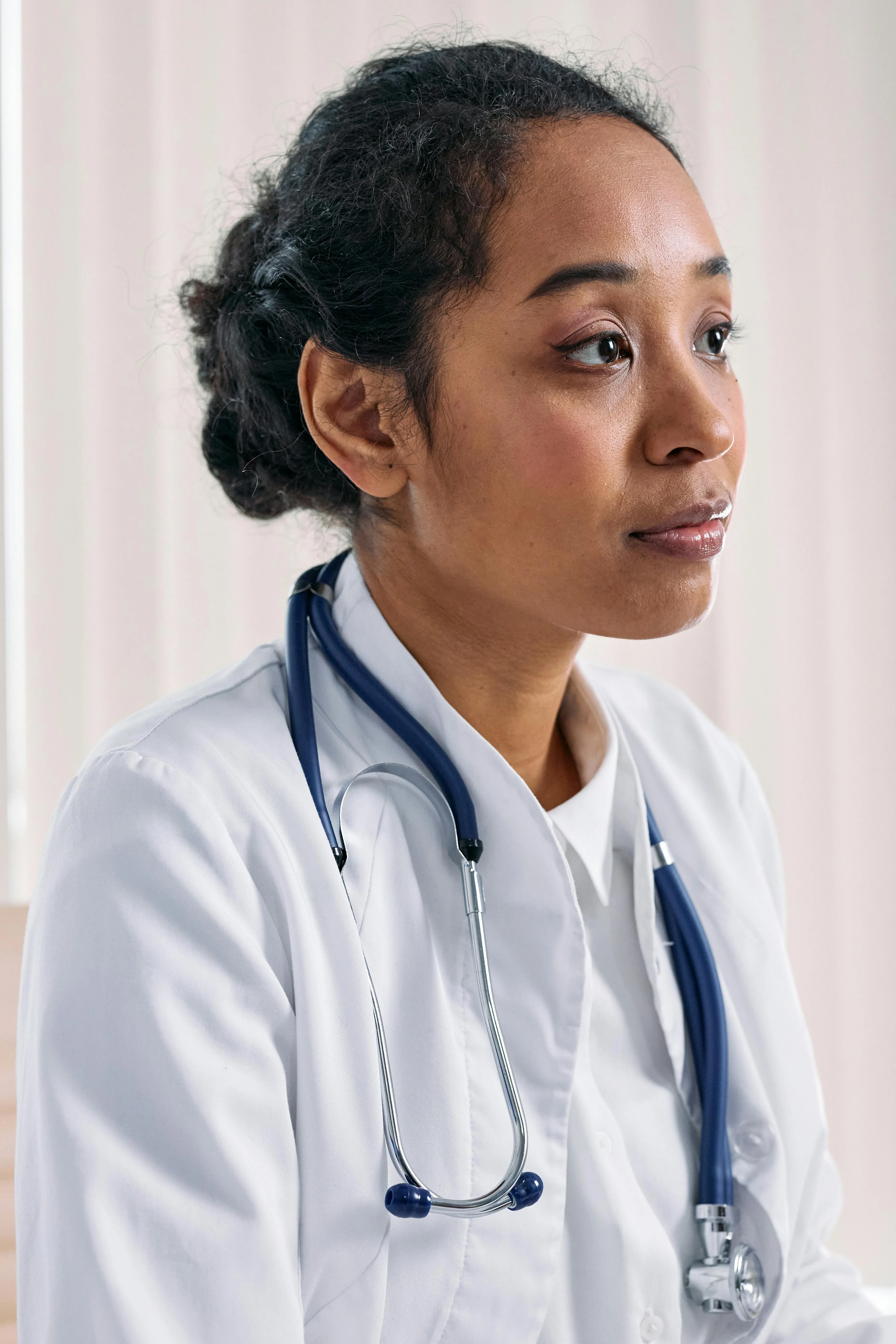 Close-up&nbsp;of&nbsp;a&nbsp;focused&nbsp;female&nbsp;doctor&nbsp;in&nbsp;a&nbsp;white&nbsp;coat&nbsp;with&nbsp;a&nbsp;stethoscope&nbsp;indoors.