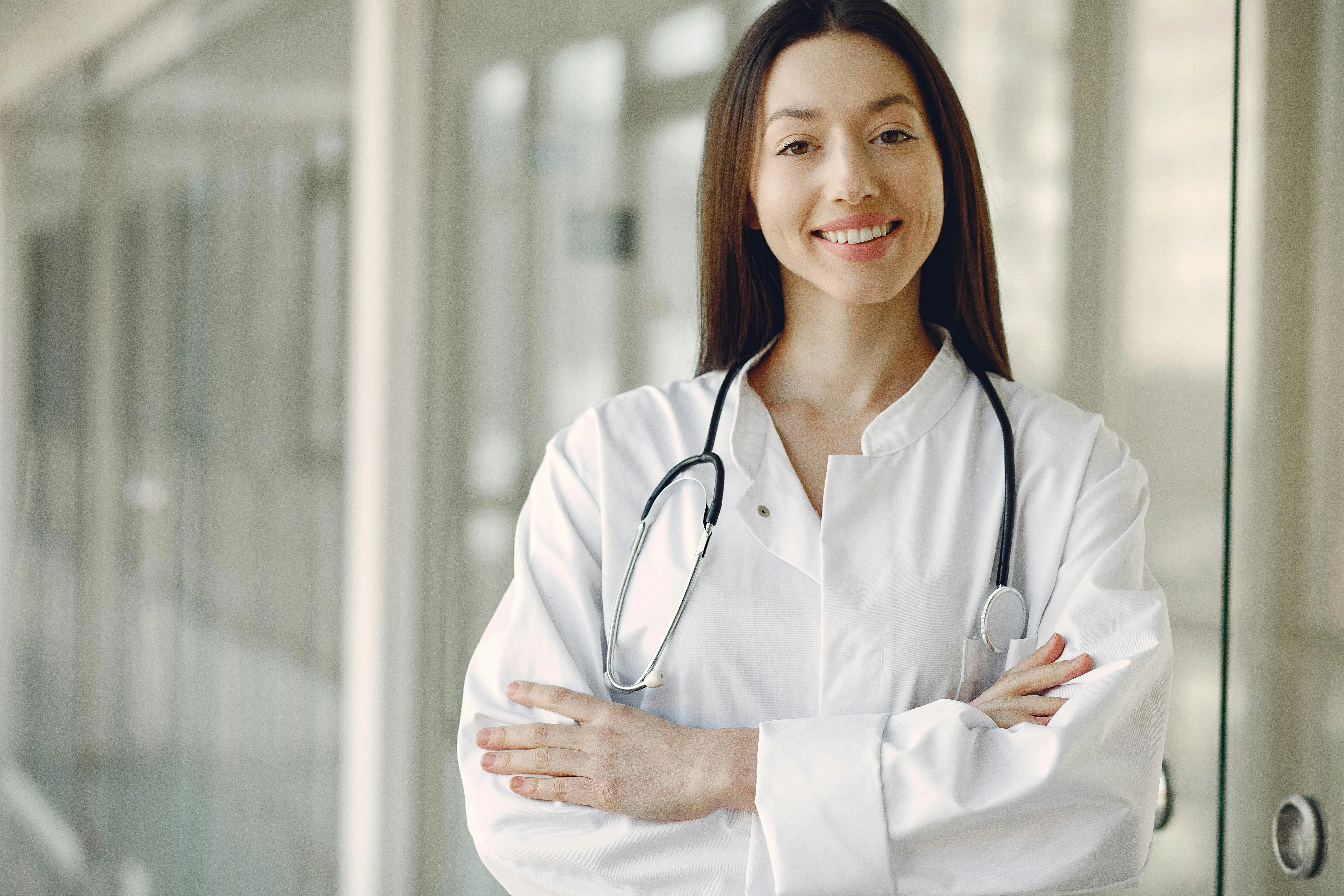 Portrait&nbsp;of&nbsp;a&nbsp;smiling&nbsp;female&nbsp;doctor&nbsp;with&nbsp;arms&nbsp;crossed&nbsp;and&nbsp;stethoscope&nbsp;in&nbsp;a&nbsp;hospital&nbsp;corridor.