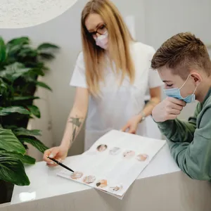 A&nbsp;healthcare&nbsp;professional&nbsp;and&nbsp;young&nbsp;man&nbsp;engaged&nbsp;in&nbsp;a&nbsp;consultation&nbsp;at&nbsp;a&nbsp;clinic,&nbsp;both&nbsp;wearing&nbsp;face&nbsp;masks&nbsp;for&nbsp;safety.