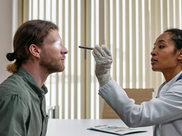 A&nbsp;doctor&nbsp;performs&nbsp;an&nbsp;eye&nbsp;examination&nbsp;on&nbsp;a&nbsp;patient&nbsp;using&nbsp;a&nbsp;flashlight&nbsp;in&nbsp;a&nbsp;clinical&nbsp;setting.