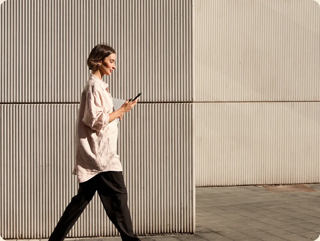 Woman walking past a ribbed wall while checking her phone