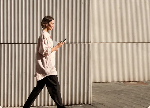 Woman walking past a ribbed wall while checking her phone