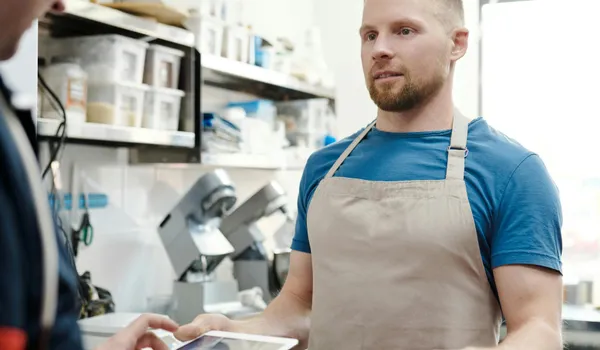 Man&nbsp;in&nbsp;apron&nbsp;holding&nbsp;thermal&nbsp;food&nbsp;bag&nbsp;preparing&nbsp;a&nbsp;delivery&nbsp;order&nbsp;in&nbsp;a&nbsp;restaurant&nbsp;kitchen.