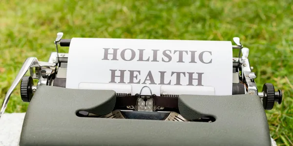 A&nbsp;vintage&nbsp;typewriter&nbsp;in&nbsp;a&nbsp;grassy&nbsp;outdoor&nbsp;setting&nbsp;displaying&nbsp;'Holistic&nbsp;Health'&nbsp;on&nbsp;paper.