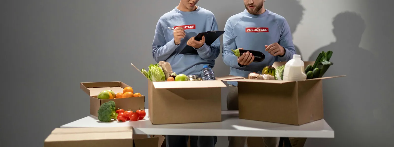 Two&nbsp;volunteers&nbsp;packing&nbsp;food&nbsp;items&nbsp;in&nbsp;cardboard&nbsp;boxes&nbsp;for&nbsp;community&nbsp;service&nbsp;indoors.