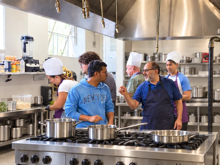 Team&nbsp;in&nbsp;chef&nbsp;hats&nbsp;cooking&nbsp;together&nbsp;in&nbsp;a&nbsp;professional&nbsp;kitchen&nbsp;during&nbsp;a&nbsp;SciCook&nbsp;team&nbsp;building&nbsp;event