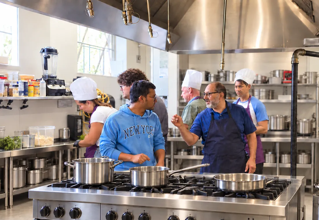 Team&nbsp;in&nbsp;chef&nbsp;hats&nbsp;cooking&nbsp;together&nbsp;in&nbsp;a&nbsp;professional&nbsp;kitchen&nbsp;during&nbsp;a&nbsp;SciCook&nbsp;team&nbsp;building&nbsp;event