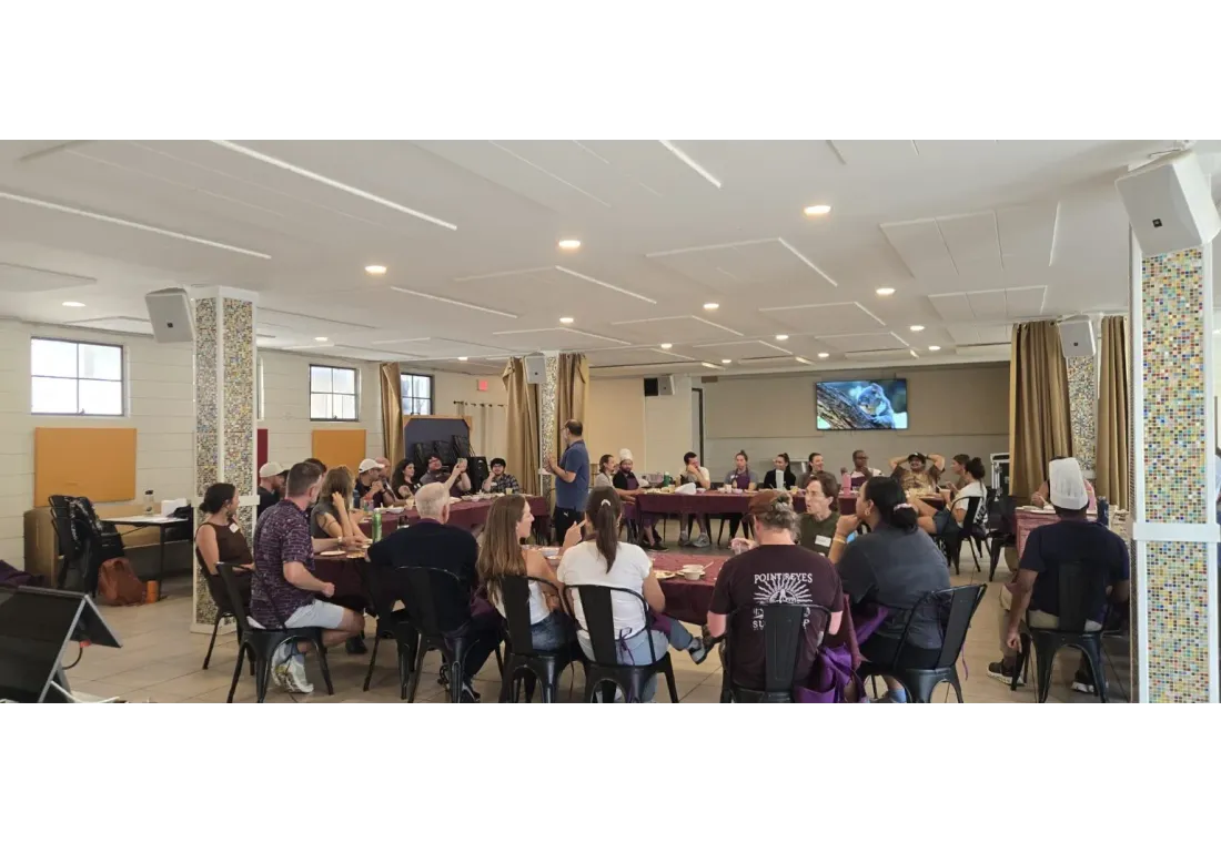 Community members seated at tables in a large hall during a SciCook nutrition and cooking workshop