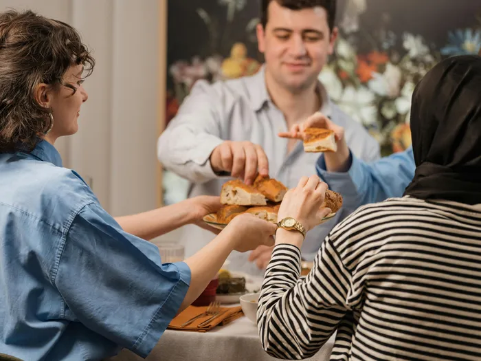 Friends&nbsp;sharing&nbsp;bread&nbsp;and&nbsp;enjoying&nbsp;a&nbsp;meal&nbsp;around&nbsp;a&nbsp;dining&nbsp;table,&nbsp;conveying&nbsp;warmth&nbsp;and&nbsp;togetherness.