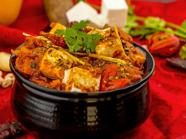 Spicy&nbsp;paneer&nbsp;tikka&nbsp;masala&nbsp;garnished&nbsp;with&nbsp;cilantro&nbsp;and&nbsp;spices&nbsp;on&nbsp;a&nbsp;vibrant&nbsp;red&nbsp;background.