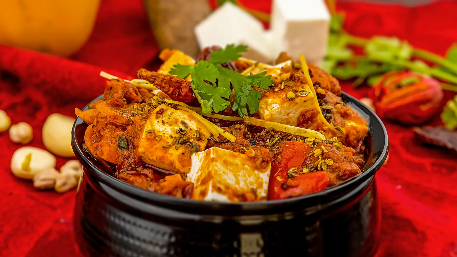 Spicy&nbsp;paneer&nbsp;tikka&nbsp;masala&nbsp;garnished&nbsp;with&nbsp;cilantro&nbsp;and&nbsp;spices&nbsp;on&nbsp;a&nbsp;vibrant&nbsp;red&nbsp;background.