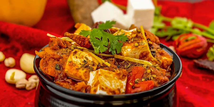 Spicy paneer tikka masala garnished with cilantro and spices on a vibrant red background.