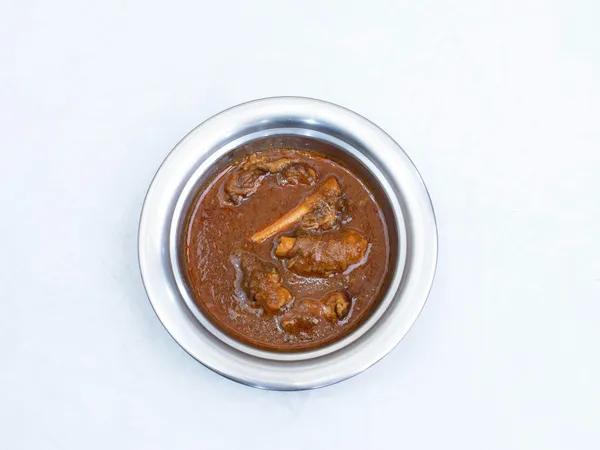 Rich&nbsp;and&nbsp;flavorful&nbsp;lamb&nbsp;curry&nbsp;served&nbsp;in&nbsp;a&nbsp;shiny&nbsp;stainless&nbsp;steel&nbsp;bowl&nbsp;on&nbsp;white&nbsp;background.