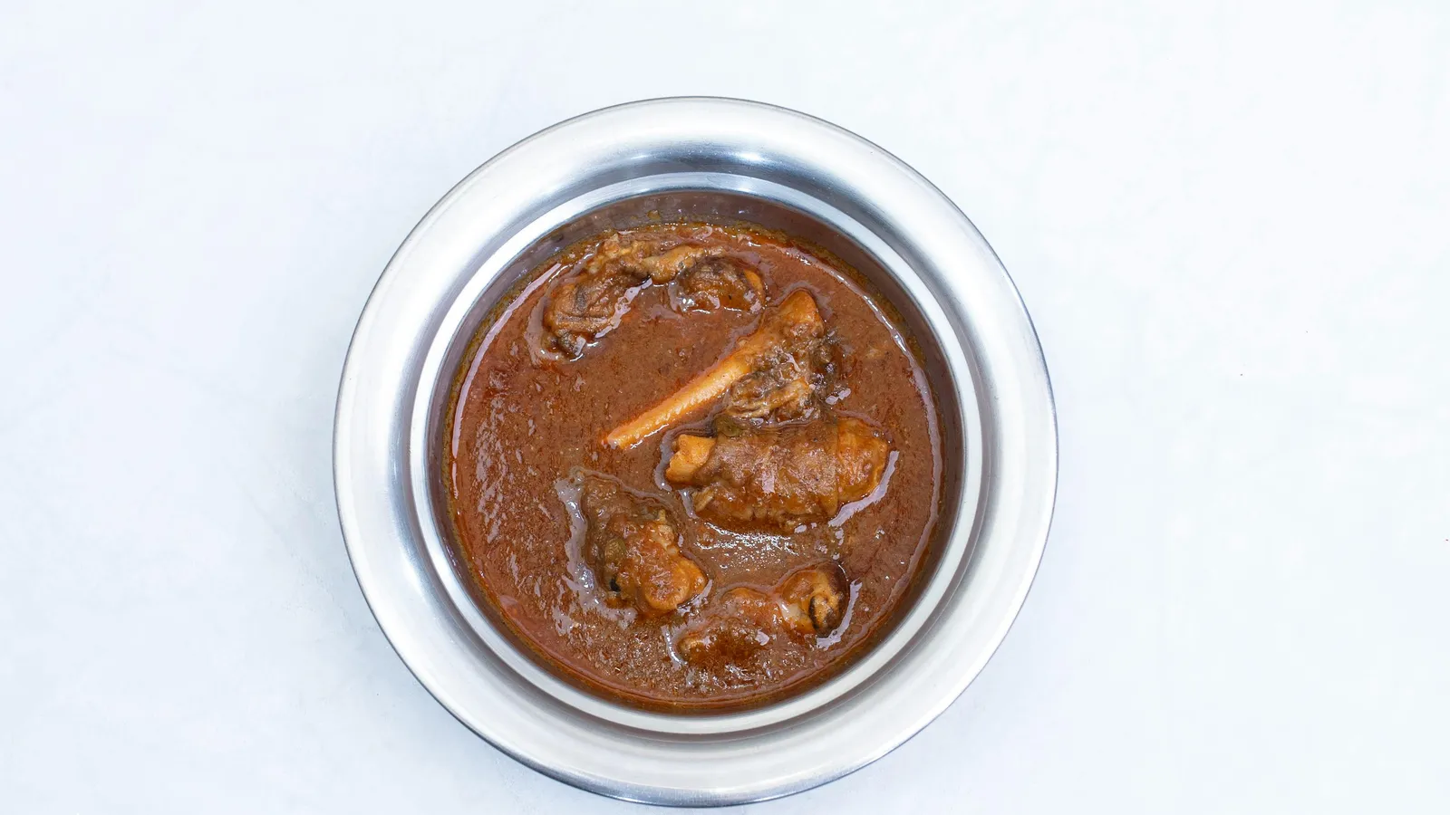 Rich&nbsp;and&nbsp;flavorful&nbsp;lamb&nbsp;curry&nbsp;served&nbsp;in&nbsp;a&nbsp;shiny&nbsp;stainless&nbsp;steel&nbsp;bowl&nbsp;on&nbsp;white&nbsp;background.