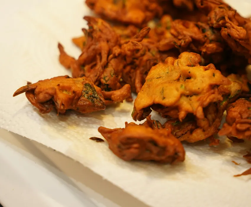 Golden&nbsp;brown&nbsp;Indian&nbsp;pakoras&nbsp;freshly&nbsp;fried&nbsp;and&nbsp;resting&nbsp;on&nbsp;paper&nbsp;towel&nbsp;in&nbsp;kitchen&nbsp;setting.