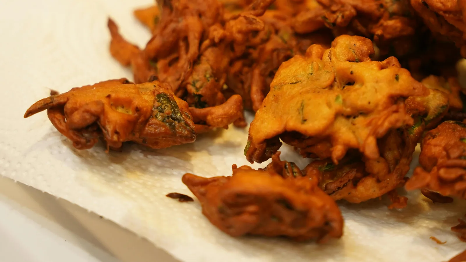 Golden&nbsp;brown&nbsp;Indian&nbsp;pakoras&nbsp;freshly&nbsp;fried&nbsp;and&nbsp;resting&nbsp;on&nbsp;paper&nbsp;towel&nbsp;in&nbsp;kitchen&nbsp;setting.