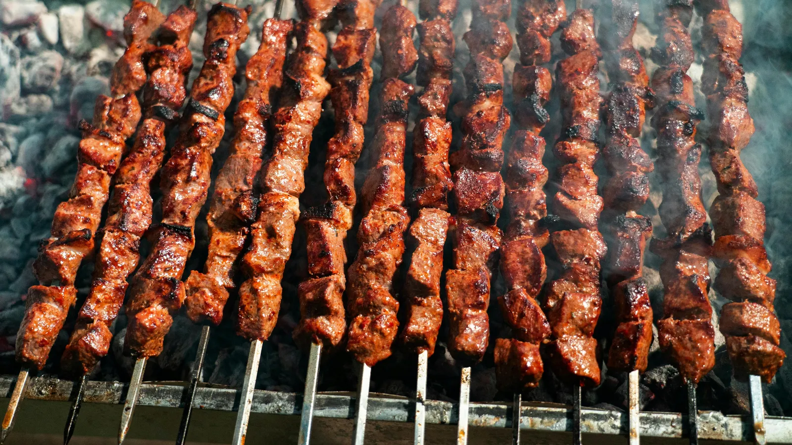 Juicy&nbsp;beef&nbsp;skewers&nbsp;sizzling&nbsp;on&nbsp;an&nbsp;open&nbsp;charcoal&nbsp;grill,&nbsp;perfect&nbsp;for&nbsp;summer&nbsp;BBQ.
