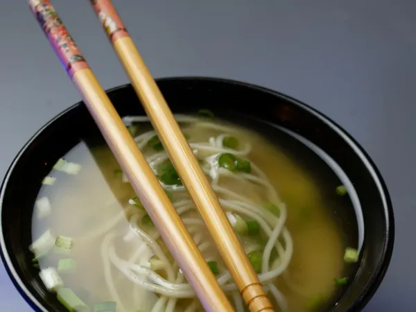 Warm&nbsp;Japanese&nbsp;soba&nbsp;noodle&nbsp;soup&nbsp;topped&nbsp;with&nbsp;scallions&nbsp;in&nbsp;a&nbsp;black&nbsp;bowl&nbsp;with&nbsp;chopsticks.