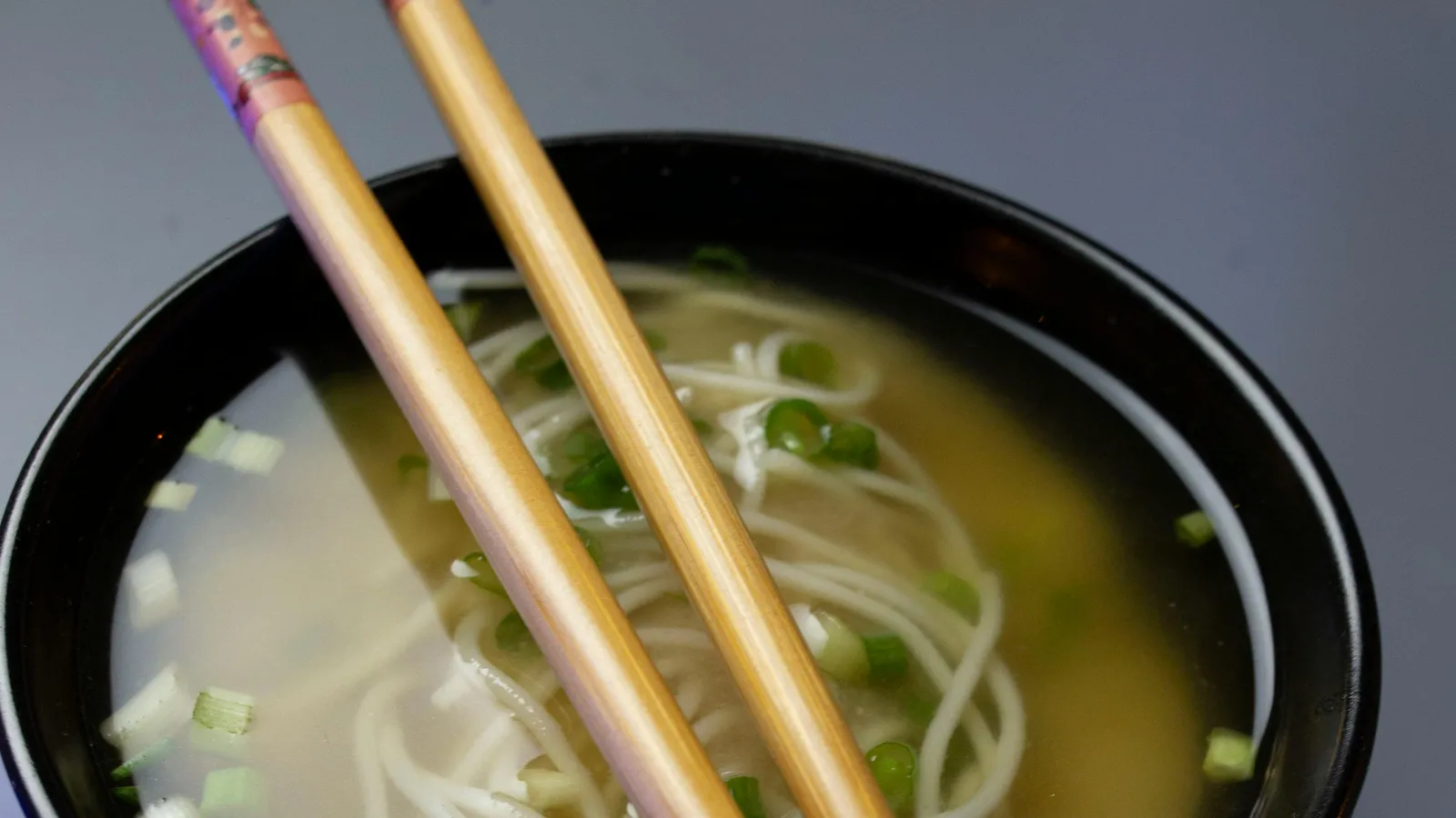 Warm&nbsp;Japanese&nbsp;soba&nbsp;noodle&nbsp;soup&nbsp;topped&nbsp;with&nbsp;scallions&nbsp;in&nbsp;a&nbsp;black&nbsp;bowl&nbsp;with&nbsp;chopsticks.