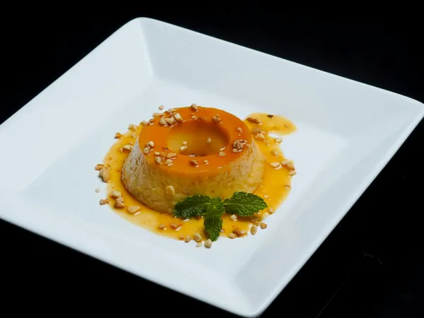 A&nbsp;beautifully&nbsp;plated&nbsp;caramel&nbsp;flan&nbsp;with&nbsp;mint&nbsp;leaves&nbsp;and&nbsp;nuts,&nbsp;set&nbsp;against&nbsp;a&nbsp;black&nbsp;background.