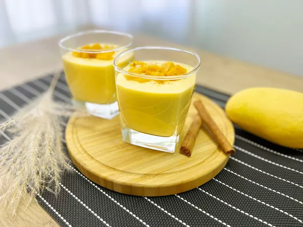Two&nbsp;glasses&nbsp;of&nbsp;creamy&nbsp;mango&nbsp;lassi&nbsp;garnished&nbsp;with&nbsp;diced&nbsp;mango&nbsp;and&nbsp;cinnamon&nbsp;sticks.
