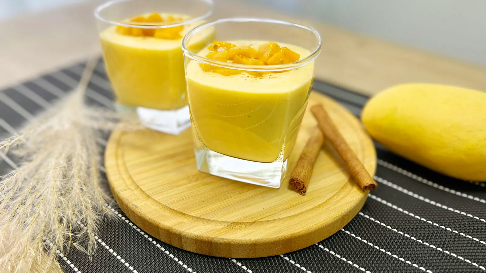 Two&nbsp;glasses&nbsp;of&nbsp;creamy&nbsp;mango&nbsp;lassi&nbsp;garnished&nbsp;with&nbsp;diced&nbsp;mango&nbsp;and&nbsp;cinnamon&nbsp;sticks.